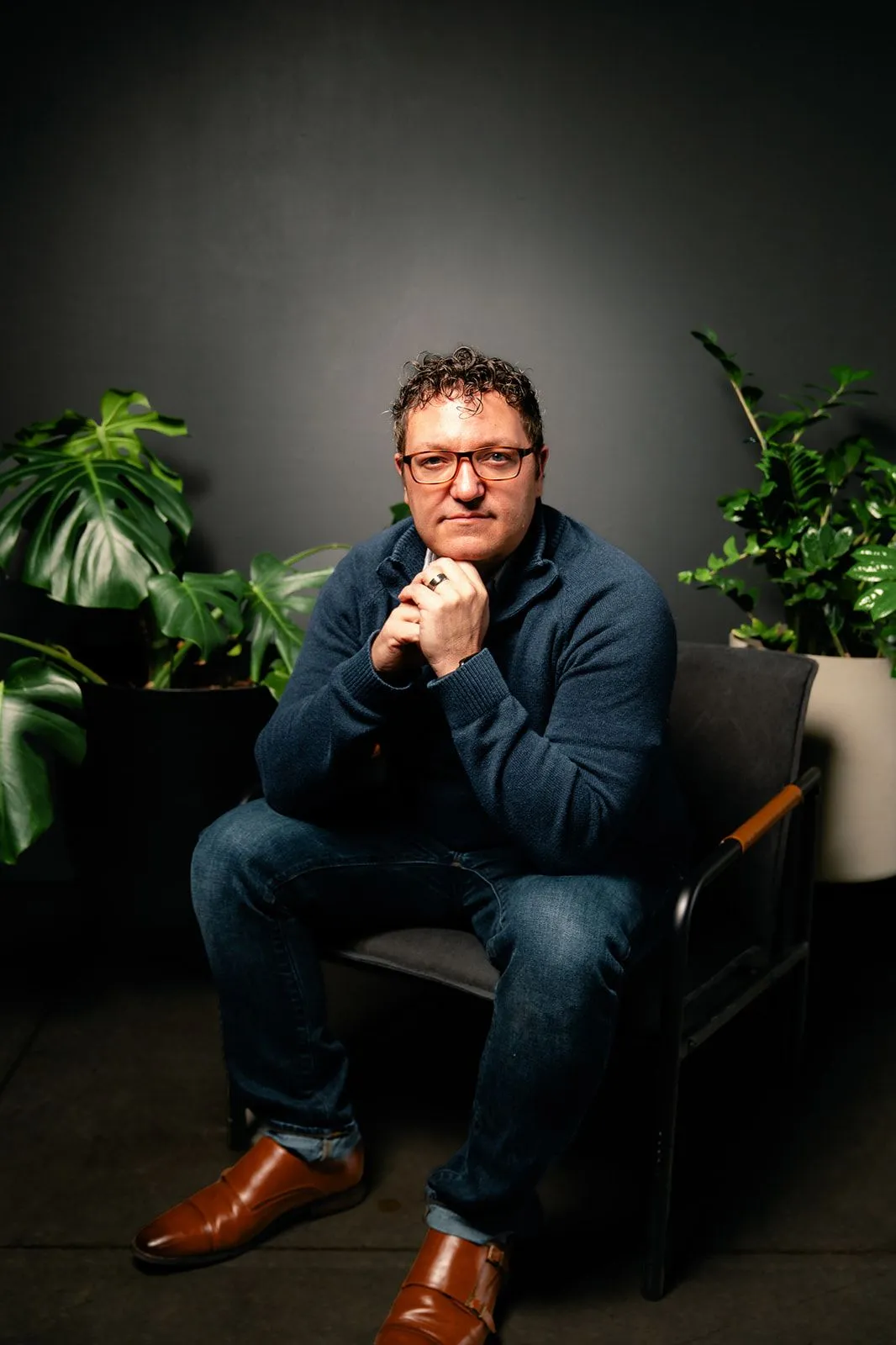Billy Mawhiney seated thoughtfully between plants against a dark background